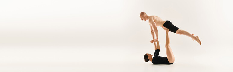 Shirtless young man and woman performing synchronized handstands in a studio setting against a...