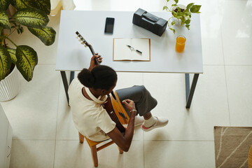 Creative Black girl sitting at desk and playing guitar, view from the top