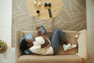 Creative Black girl drawing on tablet with digital pen when relaxing on sofa, view from the top - 782089390