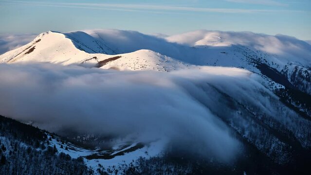 Low inversion clouds drift over snow-capped mountain peaks and hills 