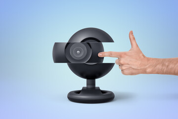 Hand pointing at a modern black webcam