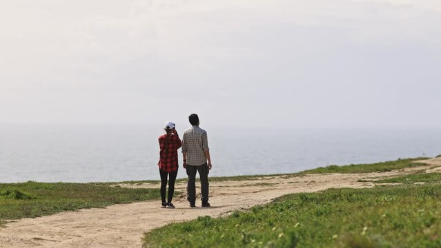 A couple is walking on a path near the ocean