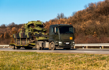 Defense, Military vehicle with caterpillar wheels, off-road armored vehicle caried by a specialized military carrier truck along the highway