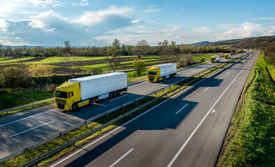 Convoy of Yellow Trucks with White containers on highway, cargo transportation concept at sunset -...