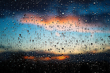 Stunning photoshoot of raindrops on a window with background of sunset in the sky. Wallpaper image with water drops and blurred sky and clouds on the background - obrazy, fototapety, plakaty
