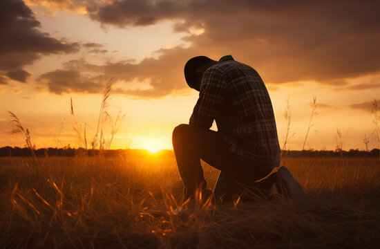 Prayer concept. Silhouette of a young man in a praying pose. On his Knees. Set against a vibrant sunset sunrise sky. Clasped hands. Also related to sacrifice, sanctification, shepherd, trinity, shadow