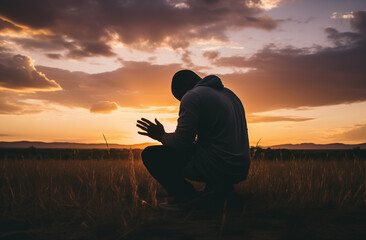 Prayer concept. Silhouette of a handsome black man in a praying pose. Set against a vibrant sunset sunrise sky. Open hands. Also related to faithful, glorify, hallelujah, immanuel, justification