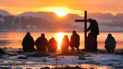 A group of people are kneeling on the beach, with a cross in the foreground
