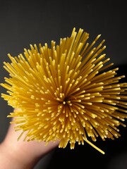 A bunch of spaghetti is held by a hand on a black background. View from above. High quality photo