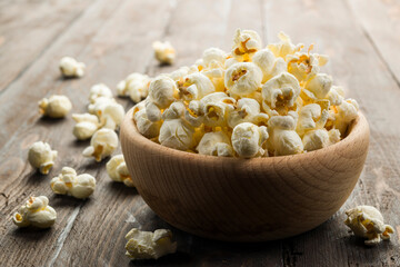 Wooden bowl with salted popcorn on wooden table.