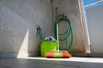 The photo shows a broom, a bucket and a mop leaning against the wall of a balcony of a house.