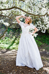 Obraz na płótnie Canvas beautiful blonde smiling romantic bride in a white dress walking in blossoming magnolia garden on sunny spring day