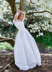 beautiful blonde smiling romantic bride in a white dress walking in blossoming magnolia garden on...