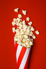 Flat lay composition with popcorn in paper cone on red background.