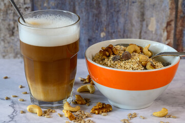 Morning meal with a bowl of oatmeal and nuts. Next to it is a glass of latte macchiato.