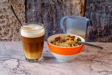 Morning meal with a bowl of oatmeal and nuts. Next to it is a glass of latte macchiato and a jug of milk.