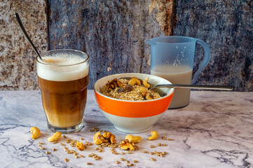 Morning meal with a bowl of oatmeal and nuts. Next to it is a glass of latte macchiato and a jug of milk.