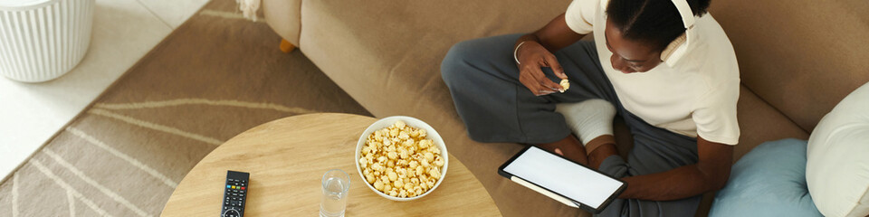 Header with Black girl eating popcorn and reading article on tablet computer - 782102515