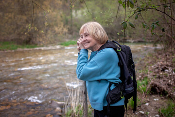 Mature woman in a teal sweater enjoying the serene ambiance by a bubbling creek in a lush forest setting, exemplifying peaceful retirement and nature connection.