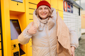 Woman receiving parcel from automatic post box using smartphone outdoors. Modern delivery technologies concept. High quality photo