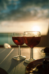 Two glasses of red wine on the table with sunset and the sea as a background