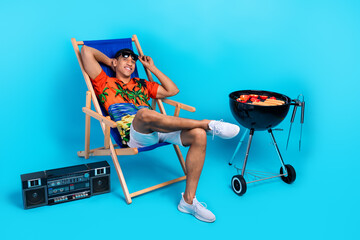 Full length photo of dreamy funky guy dressed print shirt relaxing lounge chair grilling sausages...