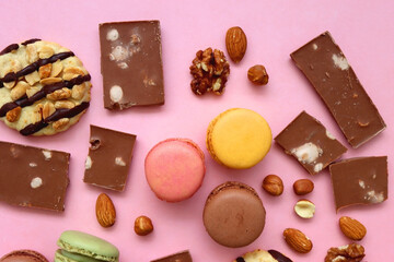 Pastel macarons, almond chocolate, peanut butter cookies and various nuts on bright pink background. Top view.