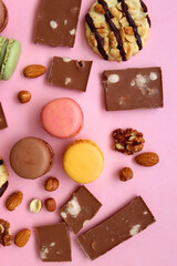Pastel macarons, almond chocolate, peanut butter cookies and various nuts on bright pink background. Top view.