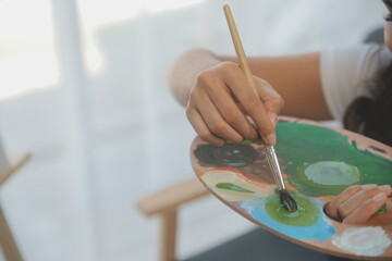 Cropped image of female artist standing in front of an easel and dipping brush into color palette
