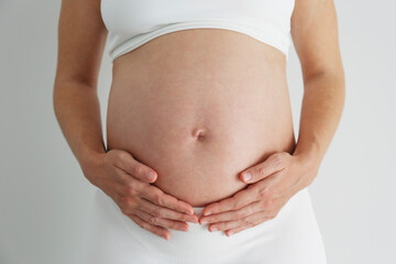 Cropped shot of pregnant woman wearing supportive maternity bra, touching her bare belly. Background, copy space, close up.