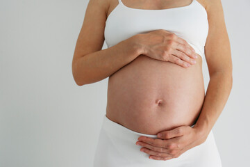 Cropped shot of pregnant woman wearing supportive maternity bra, touching her bare belly. Background, copy space, close up.