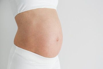 Cropped shot of pregnant woman wearing supportive maternity bra, showing her bare belly. Background, copy space, close up.