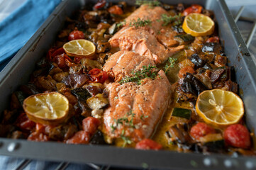 Oven baked half salmon with roasted mediterranean vegetables on a baking tray