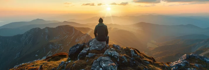 Cercles muraux Montagnes Person watching sunrise on mountain peak - A lone adventurer sits on a rugged mountain peak, facing a breathtaking sunrise that illuminates the scenic landscape