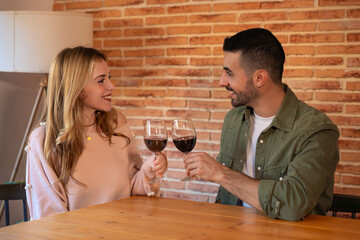  Couple clinking glasses of red wine while having a romantic date at the restaurant, celebrating Valentine's Day. Close-up of male and female hands of lovers rising for a celebratory toast