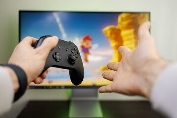 Male hands gesturing in front of the monitor holding a gamepad. Video game gamepad in hand