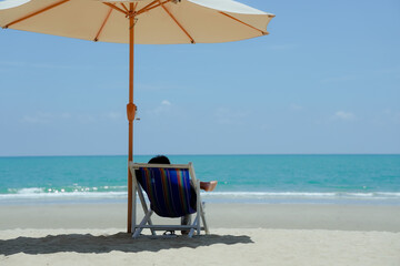 People sitting on lounge chairs on tropical beach under umbrellas, white sand, sea, chill, relax, vacation