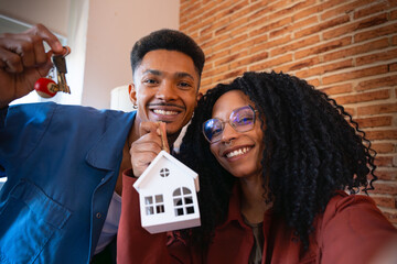  Multiracial couple showing a mini wooden house and a key with a key ring. 