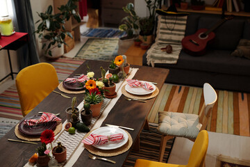 Several chairs surrounding served dinner table with domestic flowers, exotic fruits and plates with napkins standing in front of camera
