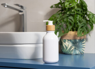 White one pump dispenser near basin and green monstera on blue countertop in bath, mockup