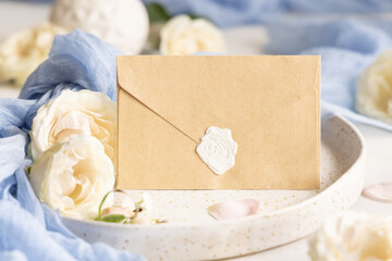 Sealed envelope near blue fabric and cream flowers on plate close up, copy space, wedding mockup