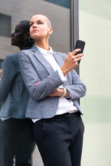  Vertical shot thoughtful Caucasian business woman using an app on her smartphone outdoors.