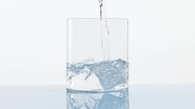 Crystal-clear water pouring into clear stylish glass wit mountain element, design isolate don white background. Concept of refreshment, aesthetics of product, health, wellness, hydration