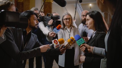 Politician answers press questions and gives interview for television breaking news. Diplomat, consul surrounded by crowd of journalists. Political speech during press conference. State of the nation. - obrazy, fototapety, plakaty
