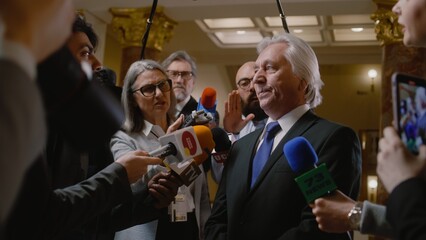 Politician answers press questions and gives interview on television political program. Senior diplomat surrounded by crowd of journalists in government building. Press conference. Hot button issues. - obrazy, fototapety, plakaty