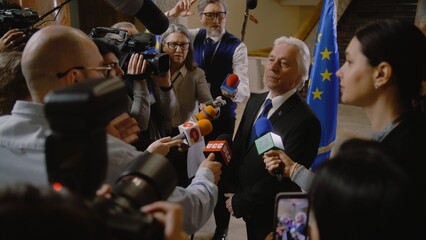EU representative answers press questions and gives interview for TV breaking news. Senior consul surrounded by crowd of journalists. Political speech during press conference. State of the nation. - obrazy, fototapety, plakaty