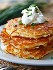 Golden homemade potato pancakes layered with sour cream and garnished with chives, on a rustic table setting.