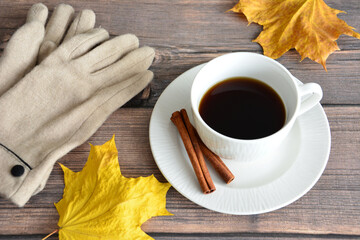 a cup of coffee with cinnamon sticks on a wooden table with yellow leaves