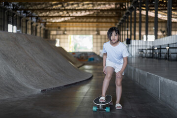 Fototapeta na wymiar surfskate by asian child skater or kid girl fun playing skateboard or ride carving surf skate to wave bank ramp in indoor skate park by summer extreme sports surfing to wears white t-shirt and sandals