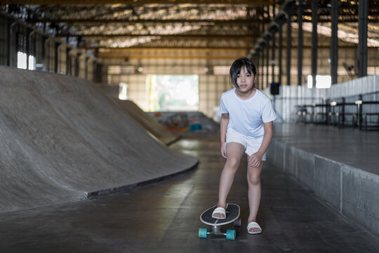 surfskate by asian child skater or kid girl fun playing skateboard or ride carving surf skate to wave bank ramp in indoor skate park by summer extreme sports surfing to wears white t-shirt and sandals